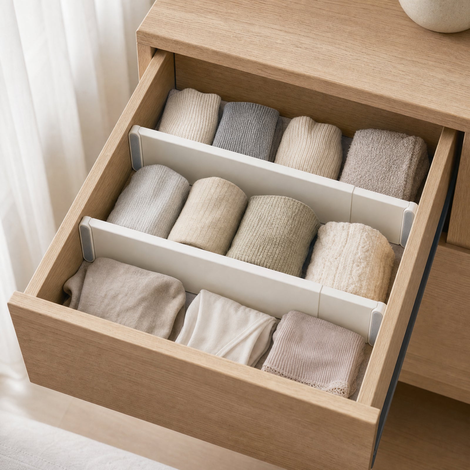 Two adjustable dividers separating folded clothing inside a light-wood drawer